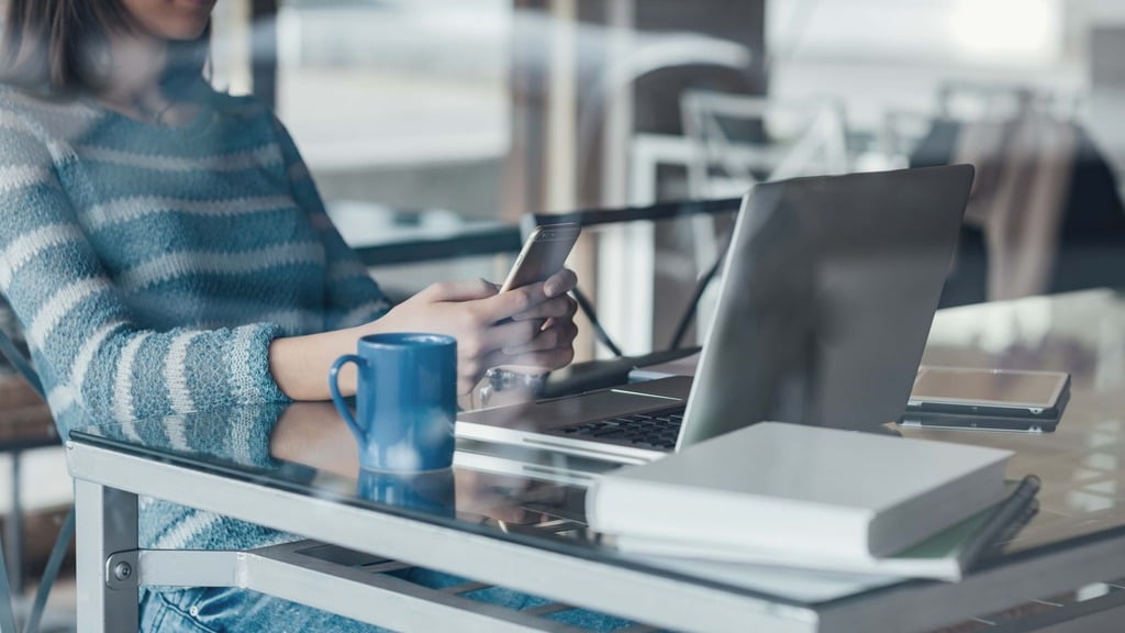 compatibilité mobile Femme qui travaille devant un ordinateur avec un téléphone à la main